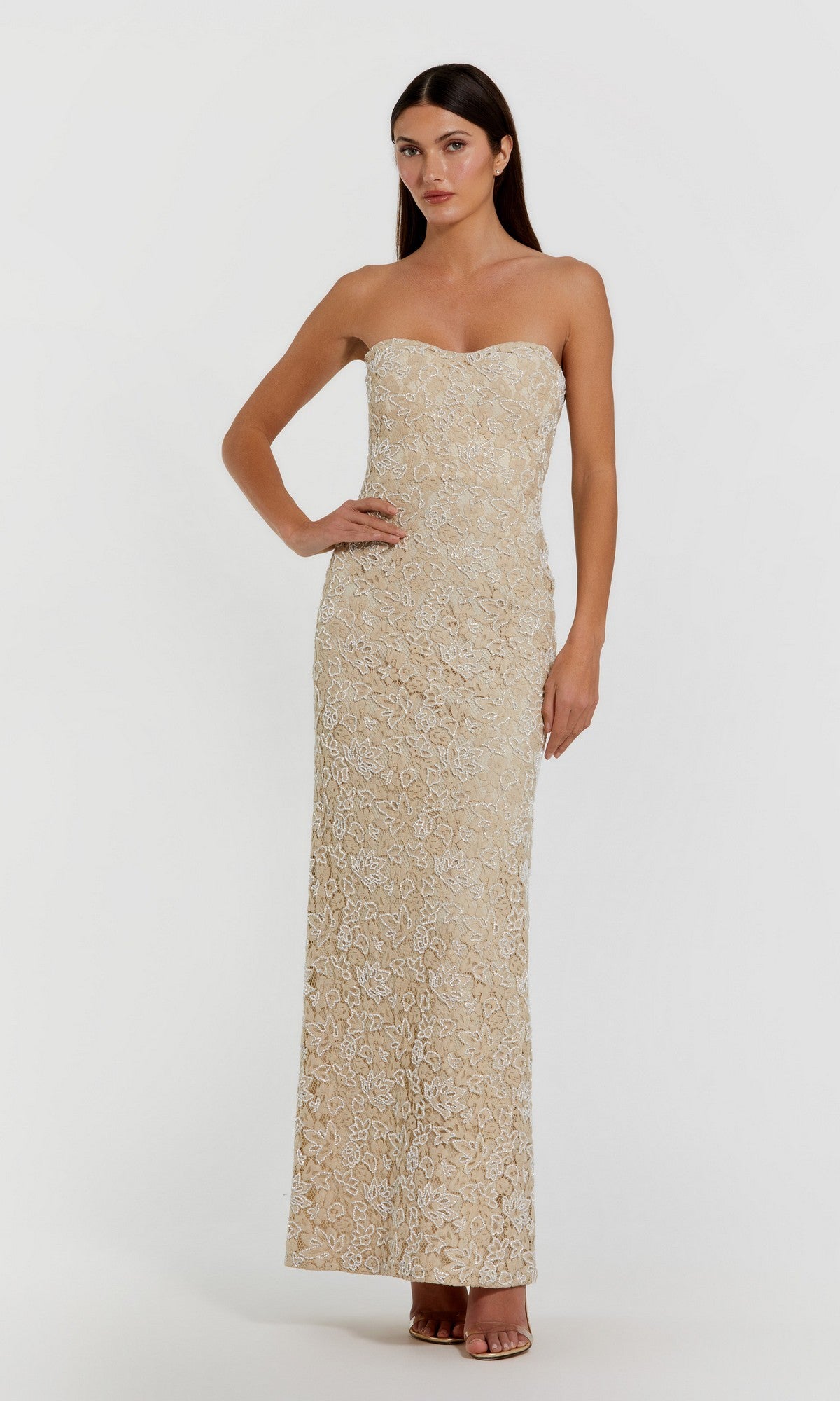 Woman wearing the beige Long Formal Dress: Mac Duggal 24067, featuring a strapless beaded lace column design with white floral detailing, stands against a plain white background.